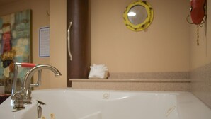 A bathroom with a large white bathtub, a silver faucet, a mirror, and a towel rack.