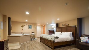 A bedroom with a large bed, a wooden dresser, a vanity with a mirror, and a bathtub.