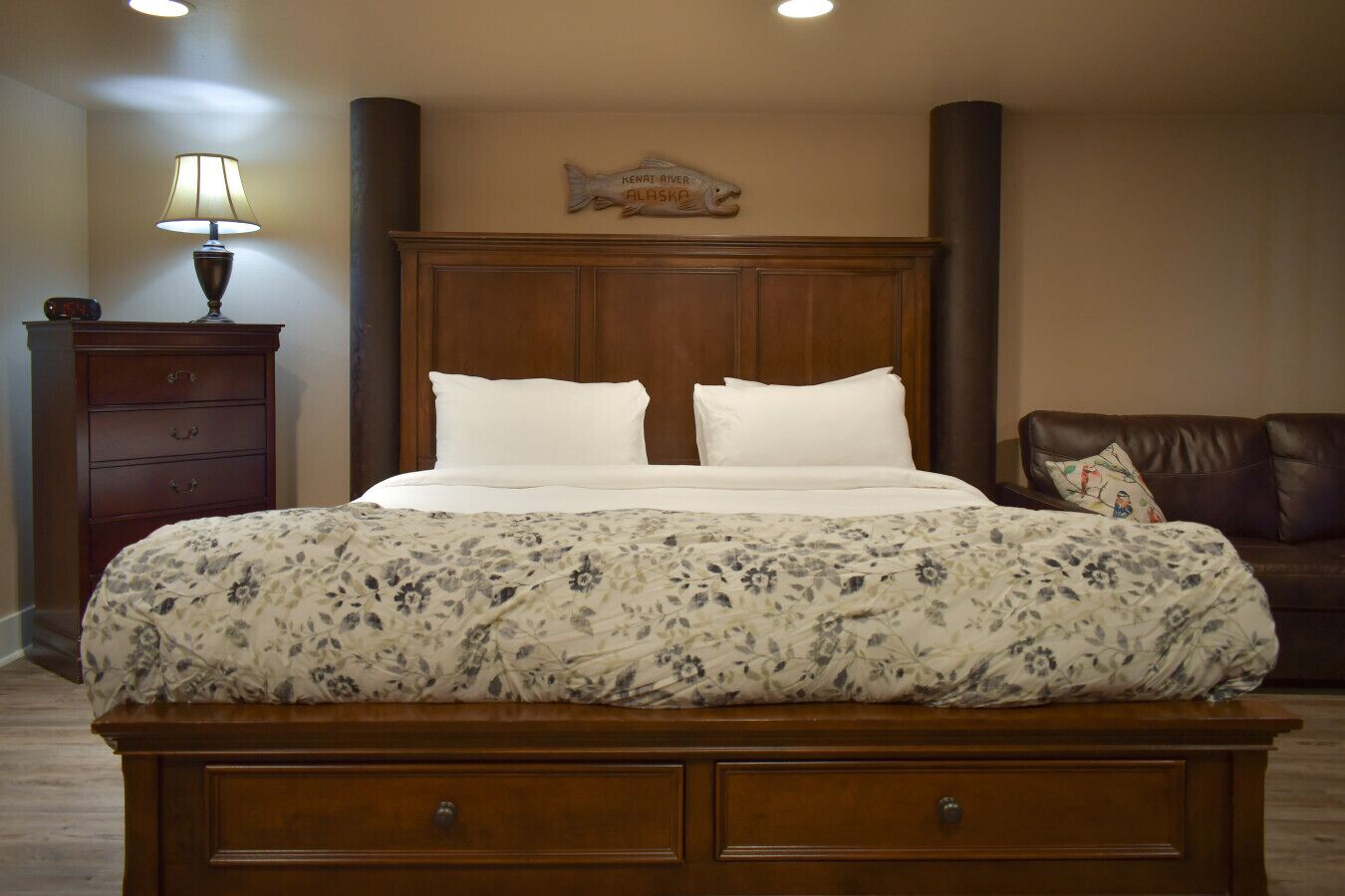 A neatly made bed with a floral bedspread, a wooden headboard, and a nightstand with a lamp.