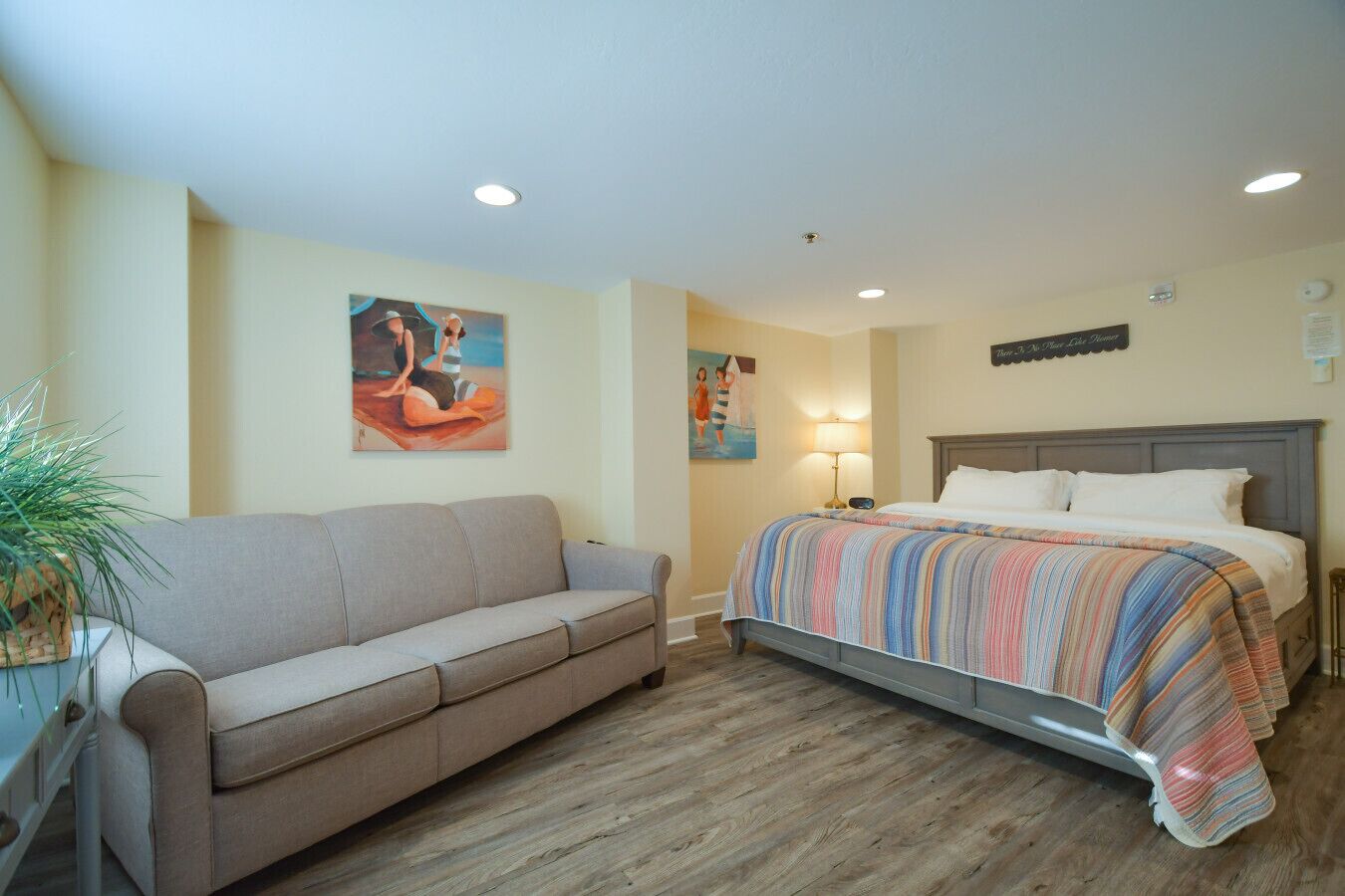 A bedroom with a bed, a sofa, a painting on the wall, and a lamp.