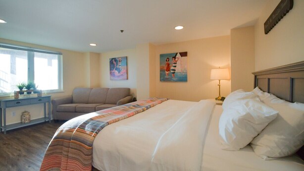 Quarto de hotel com cama, sofá, escrivaninha com luminária e obras de arte nas paredes.