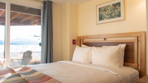 Ett hotellrum med en säng, ett fönster med utsikt över bergen, en stol och en tavla på väggen.