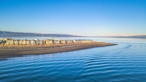 A coastal hotel with a row of ocean-facing rooms, a sandy beach, and a clear view of the sea.
