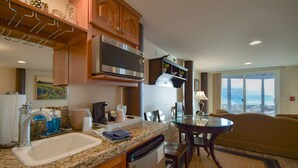 A modern kitchen with a microwave, sink, and coffee maker. There's a dining area with a table and chairs, and a view of the ocean through large windows. - Lakeshore Lodging Ocean Front Lodges (Homer)