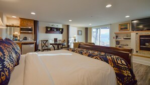 A hotel room with a large bed, a desk, a television, and a view of the ocean. - Lakeshore Lodging Ocean Front Lodges (Homer)