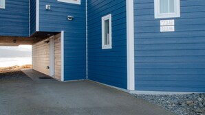 A blue building with a garage door, a number plaque, and a view of the water. - Lakeshore Lodging Ocean Front Lodges (Homer)