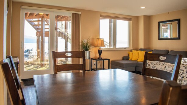 Un coin repas avec une table et des chaises, un canapé avec des coussins, une lampe et, vue à travers une porte, une terrasse extérieure.