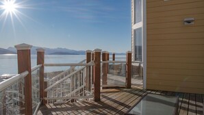 A deck with a railing, a glass door, and a view of a body of water and mountains.