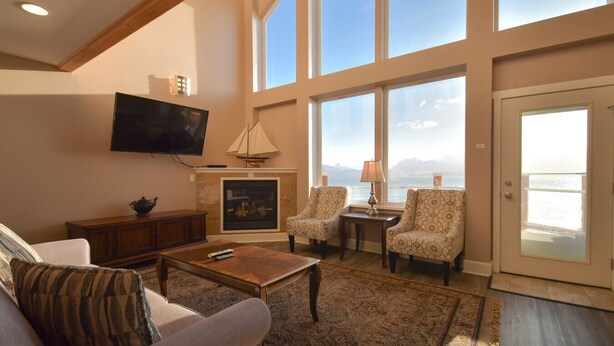 A spacious living room with a fireplace, comfortable seating, a television, and large windows offering a view of the outdoors.