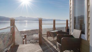 Una terraza de madera con barandilla de cristal que da a un lago y montañas.