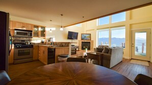 A modern kitchen with wooden cabinets, a dining table, and a fireplace. - Lakeshore Lodging Lodge 713 (Homer)