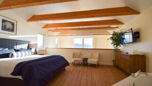 A bedroom with a bed, two chairs, a dresser, a TV, and a large window. - Lakeshore Lodging Lodge 713 (Homer)