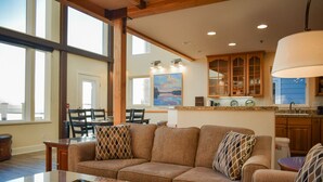 A spacious living room with a large sofa, a dining area with chairs, and a kitchen with wooden cabinets. - Lakeshore Lodging Lodge 715 (Homer)