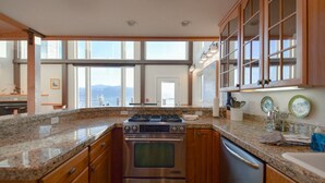A kitchen with granite countertops, stainless steel appliances, wooden cabinets, and large windows offering a view. - Lakeshore Lodging Lodge 715 (Homer)
