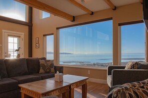 A living room with a large window overlooking a body of water, a wooden table, and a couch.