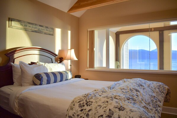 A bedroom with a bed, pillows, a lamp, and a window with a view.
