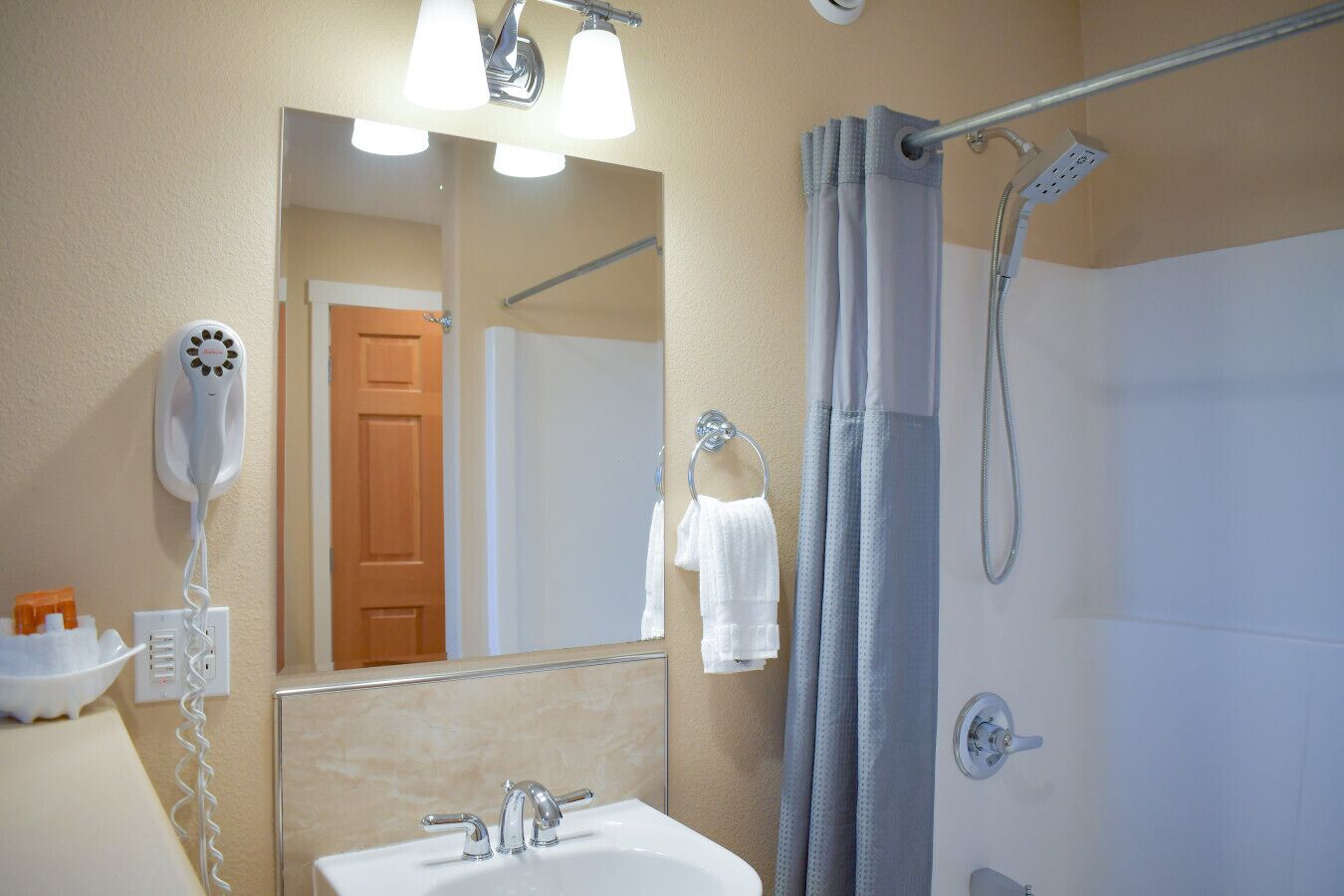 A bathroom with a sink, mirror, hairdryer, shower, and towel rack.