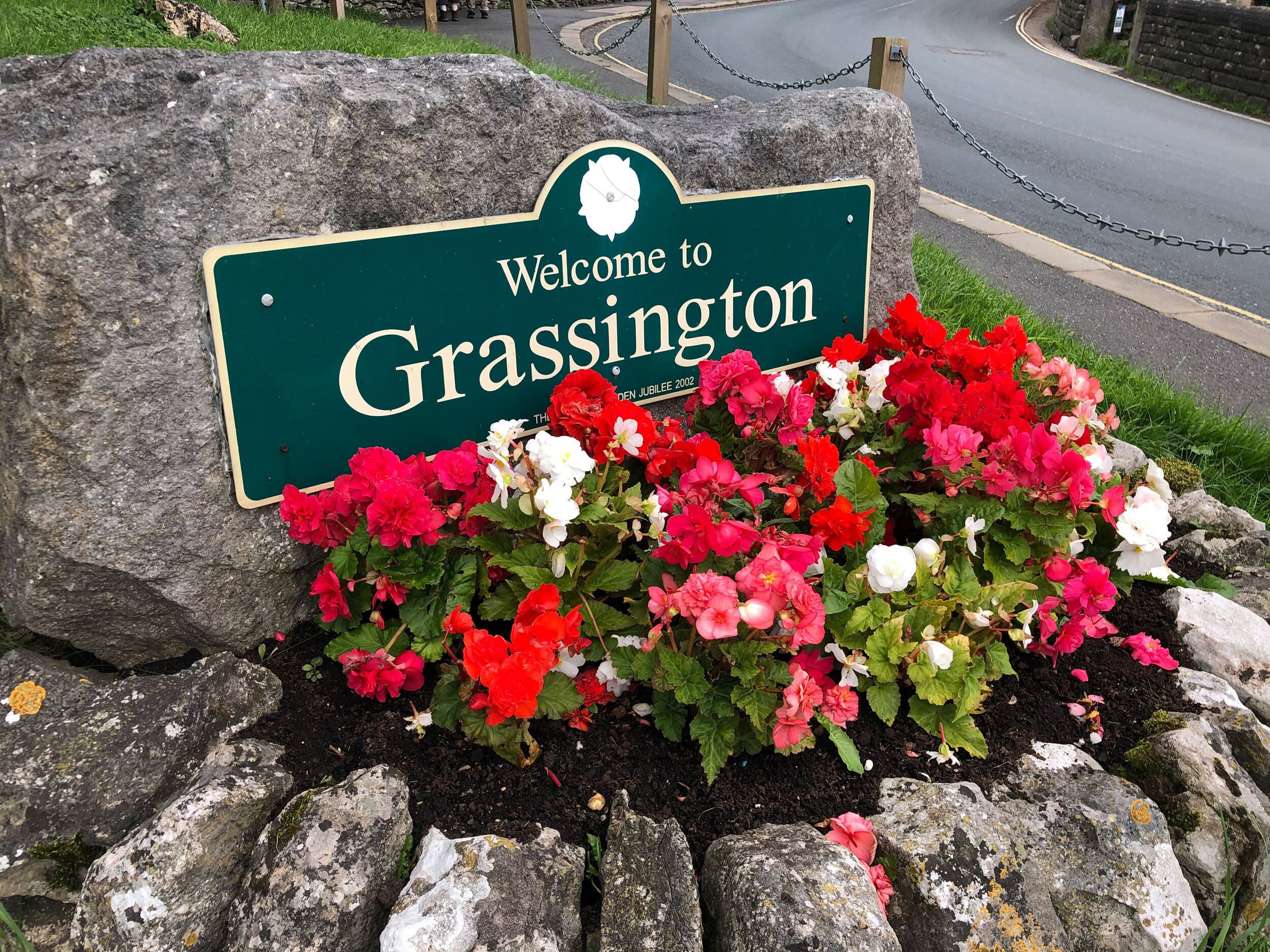 A welcome sign for Grassington with a flower bed in front.