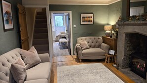 Ein gemütliches Wohnzimmer mit Kamin, einer Couch, einem Sessel und einer Treppe, die in einen anderen Raum führt.