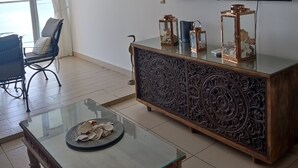 Un soggiorno moderno con un tavolino in vetro, una poltrona, una TV a parete e soprammobili su un mobile in legno.