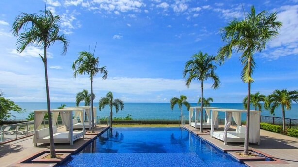 Una piscina con vista sull'oceano, circondata da palme e sdraio.