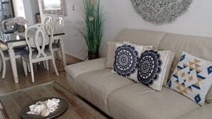 Un soggiorno con un divano beige, cuscini decorati, un tavolino in legno e un elemento decorativo a parete.
