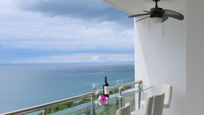 Un balcone con un tavolo in vetro, due sedie bianche, una bottiglia di vino e un bicchiere di vino.