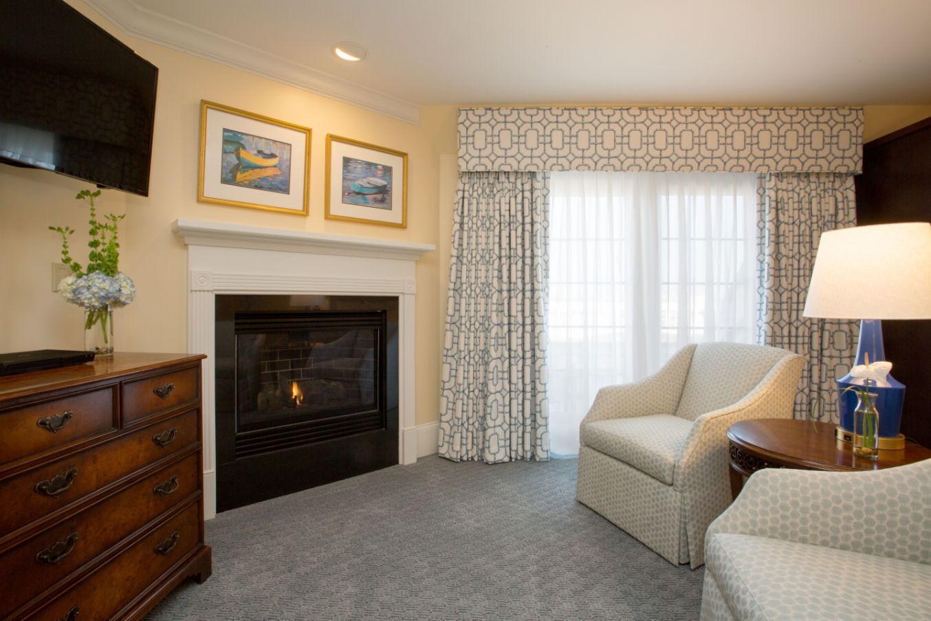 A hotel room with a fireplace, a sofa, a chair, a TV, and patterned curtains.