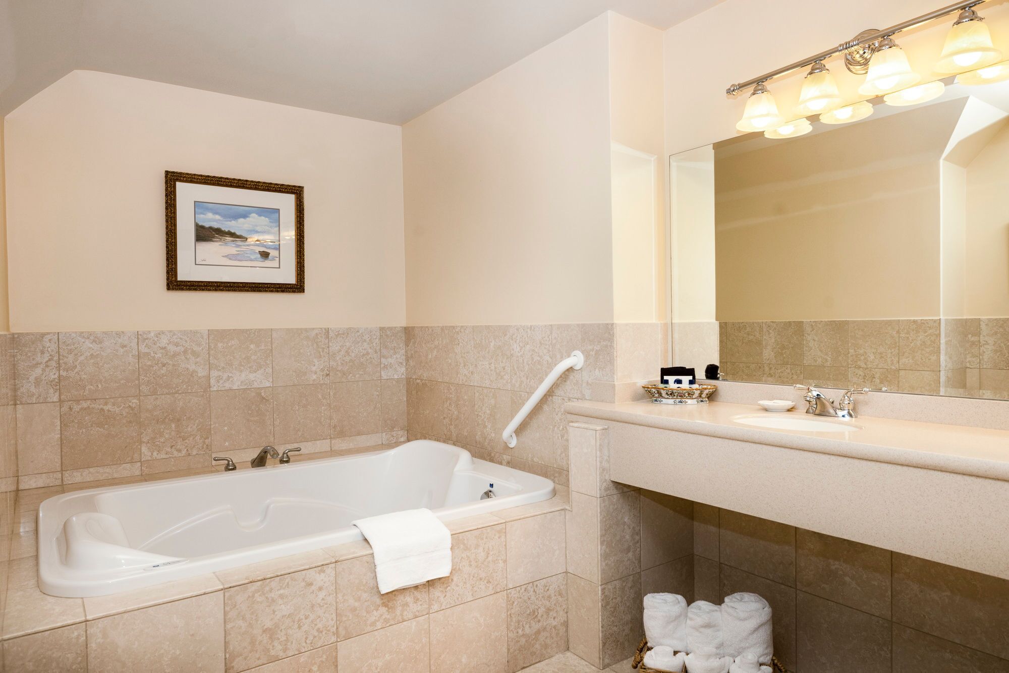 Une salle de bain avec une baignoire, un lavabo, un miroir, un porte-serviettes et un tableau encadré au mur.