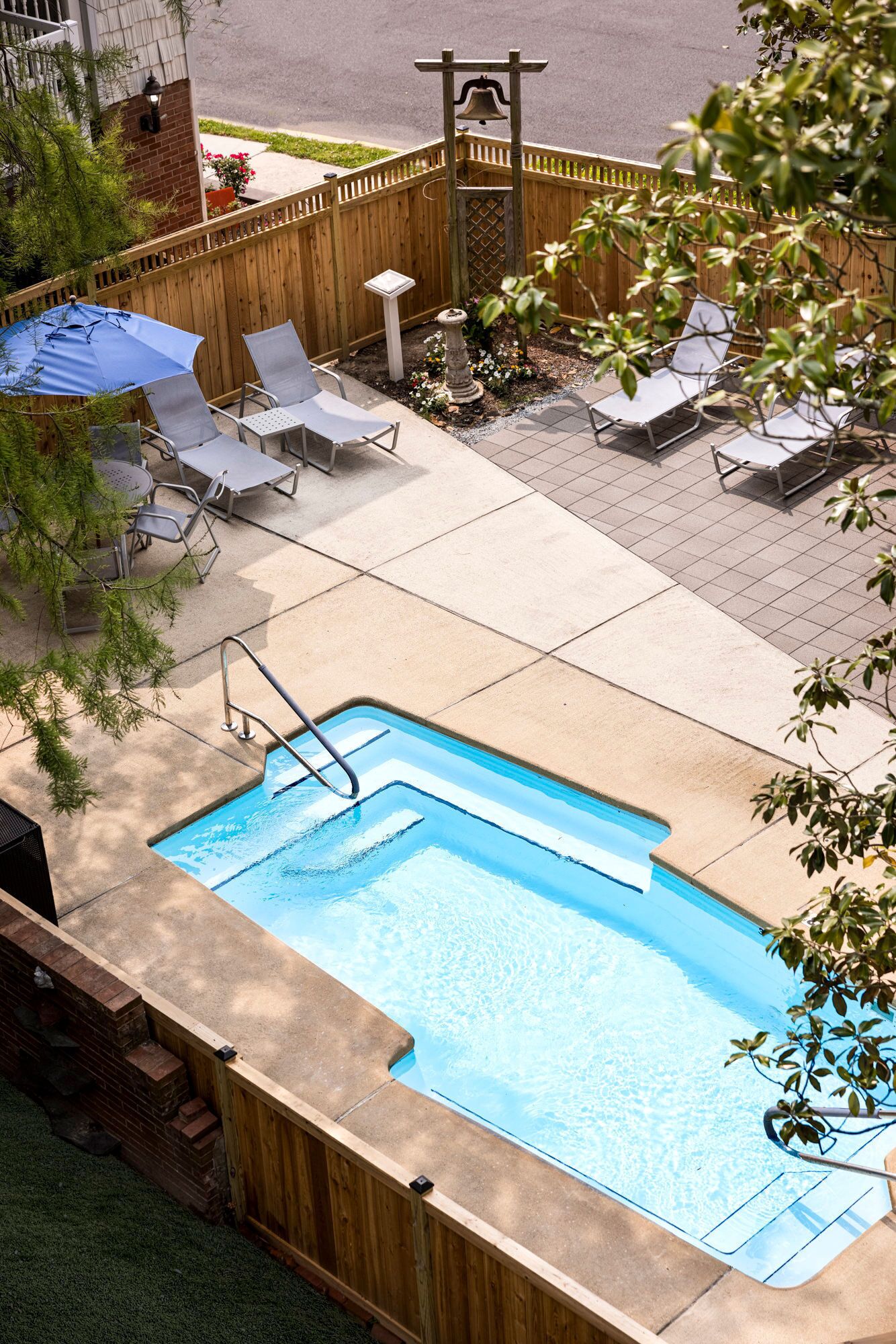 Une piscine rectangulaire entourée d’une terrasse en bois, dotée d’un escalier et bordée de chaises longues et d’un petit jardin.