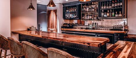 A bar area with wooden bar counters, hanging pendant lights, and a variety of liquor bottles on shelves.