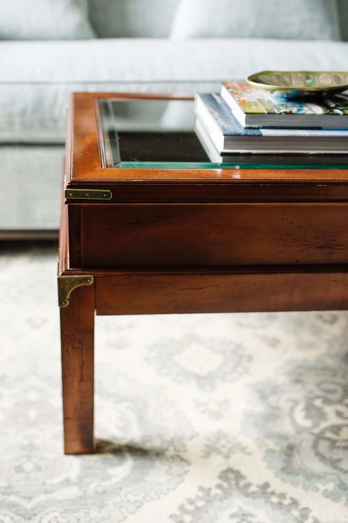A wooden coffee table with a glass top, placed on a patterned rug.