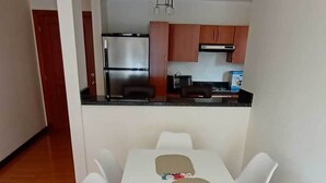 Un comedor con una mesa y sillas blancas, una cocina al fondo y suelo de madera.