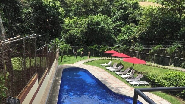 Una piscina con valla perimetral, sillas de descanso y sombrillas.