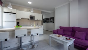 A modern kitchen with white cabinets, a central island with bar stools, a purple sofa, and a coffee table. - Beachfront Apartment in Playa de Mogan (Mogan)