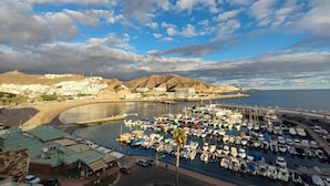 A marina with numerous boats docked, a beach, and buildings in the background. - Beachfront Apartment in Playa de Mogan (Mogan)