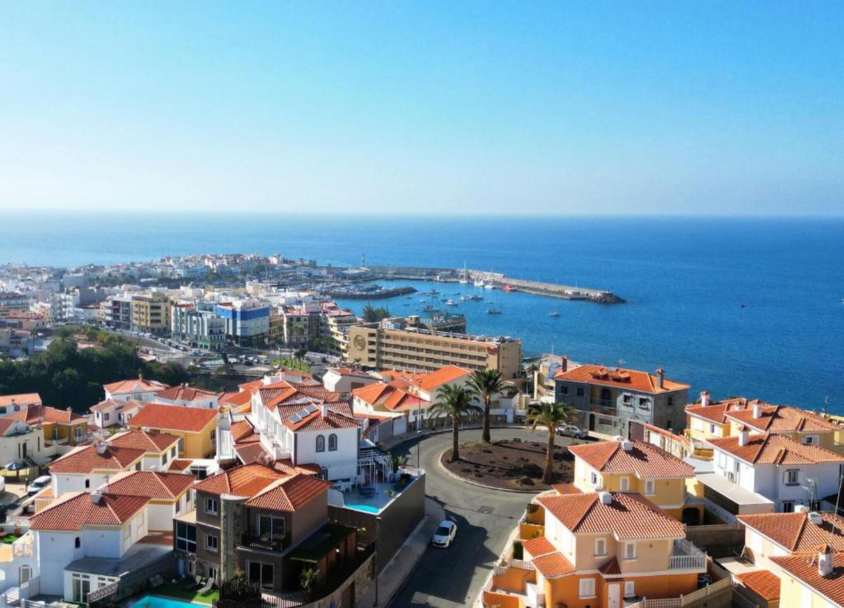 A coastal town with terracotta-roofed buildings, a marina, and a clear view of the sea.