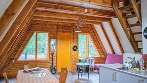 A cozy attic room with wooden beams, a dining table with chairs, a drum set, and a kitchenette.