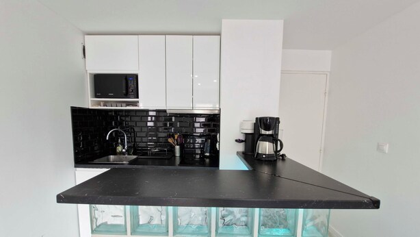 Een kleine keuken met witte kasten, een zwart aanrecht, een magnetron en een koffiezetapparaat.
