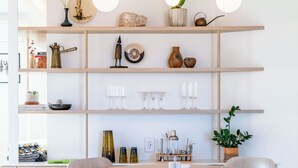A modern dining area with a round wooden table, white chairs, and a shelf with various decorative items. - Stylish, Secluded, Peaceful Home with Hot Tub, EV Charger, Star Gazing (Yucca Valley)