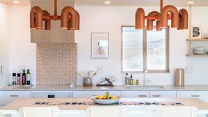 A modern kitchen with a large island, pendant lights, a window with a view, and various kitchen items. - Stylish, Secluded, Peaceful Home with Hot Tub, EV Charger, Star Gazing (Yucca Valley)