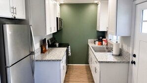 A narrow kitchen with white cabinets, a stainless steel refrigerator, a microwave, and a stove.