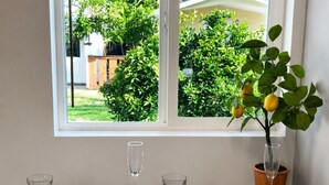 A dining table set for two with plates, cutlery, and glasses, positioned in front of a window with a view of greenery.