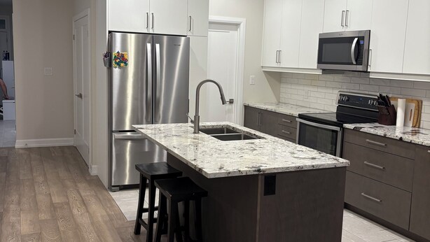 Una cocina moderna con un refrigerador de acero inoxidable, un microondas integrado y una isla de granito con taburetes de bar.