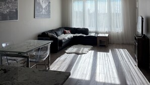 Una sala moderna con un sofá de cuero negro, una mesa de comedor de cristal y una alfombra blanca y mullida.
