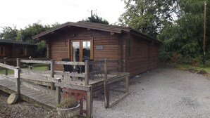 A wooden cabin with a covered deck and a gravel driveway. - Hand Built log Cabin at Avonvale Holiday Lodges (Evesham)