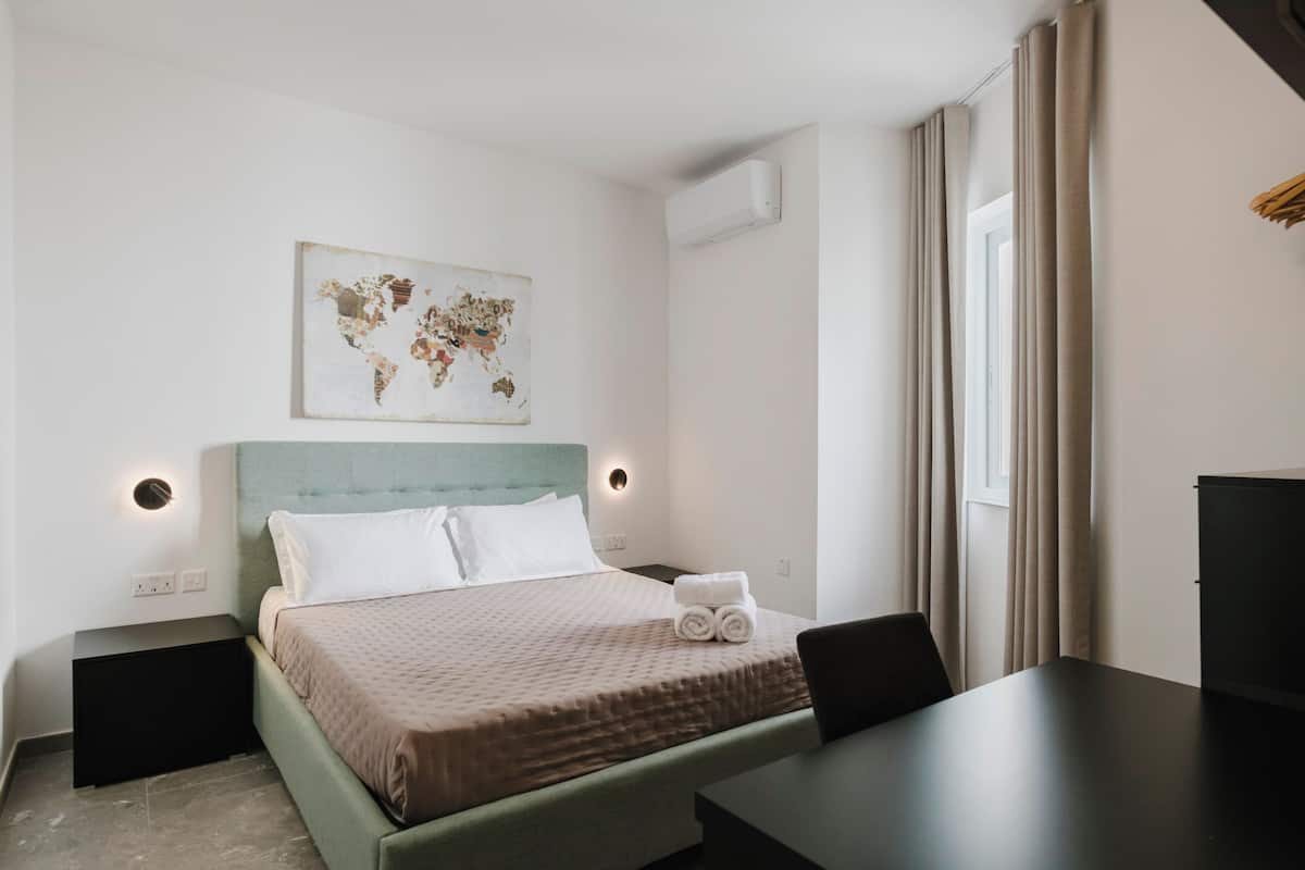 Une chambre d’hôtel bien rangée, avec un lit, des tables de chevet, un bureau et une œuvre d’art représentant une carte du monde accrochée au mur.