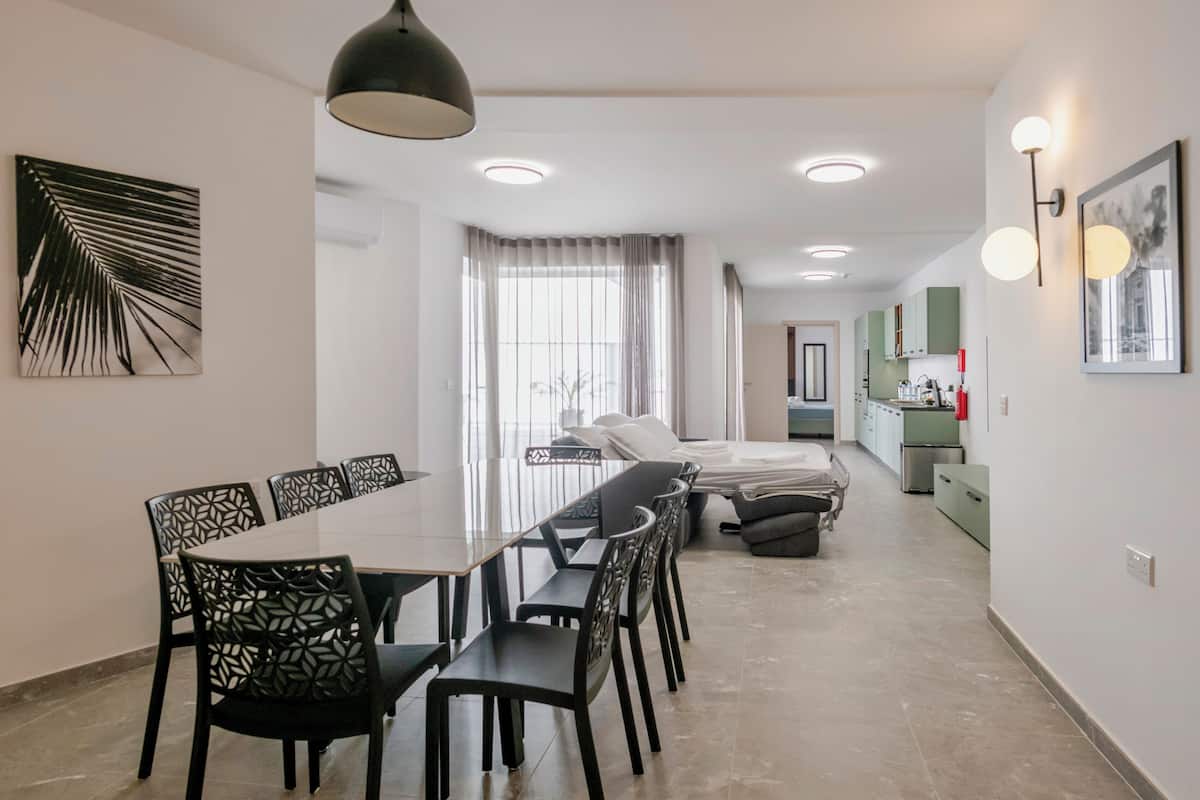 Un espace de repas moderne avec une longue table et des chaises, un canapé et une cuisine en arrière-plan.