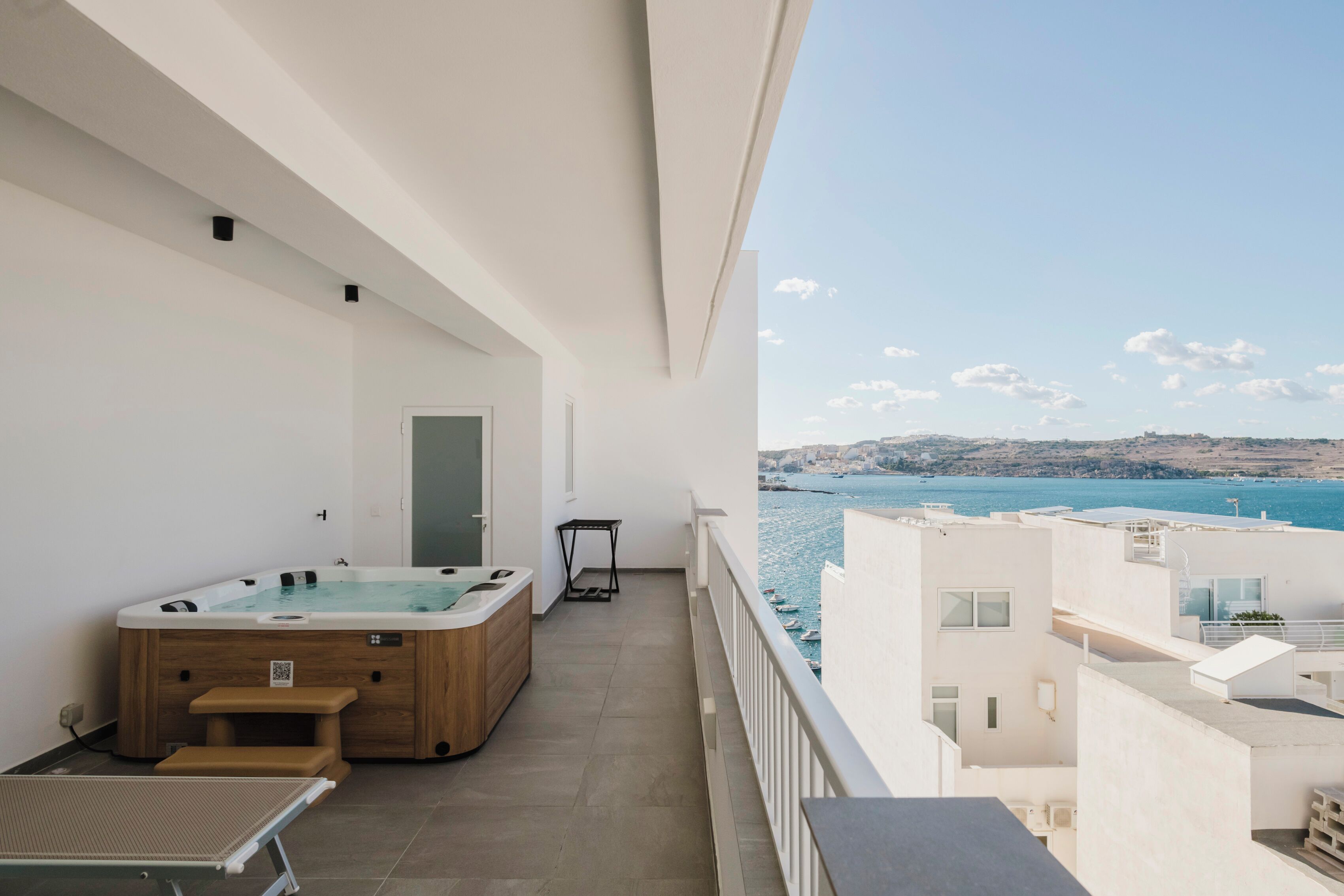 Un balcone con vasca idromassaggio, un tavolo e vista sul mare.