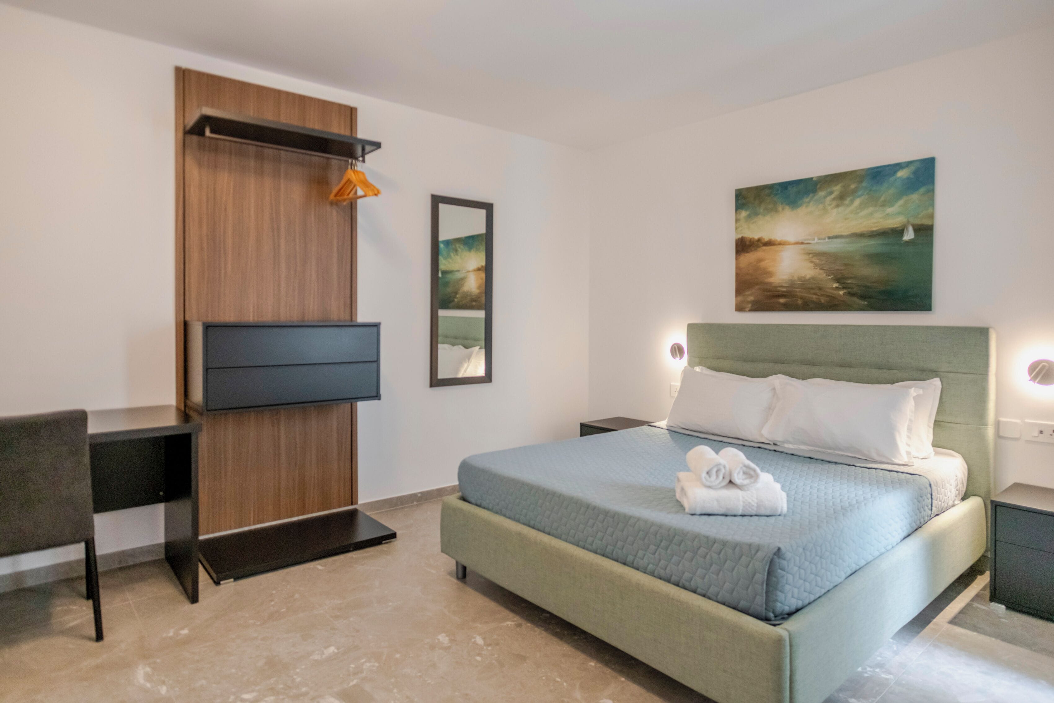 Une chambre d’hôtel moderne avec un grand lit, un bureau et un téléviseur fixé au mur.